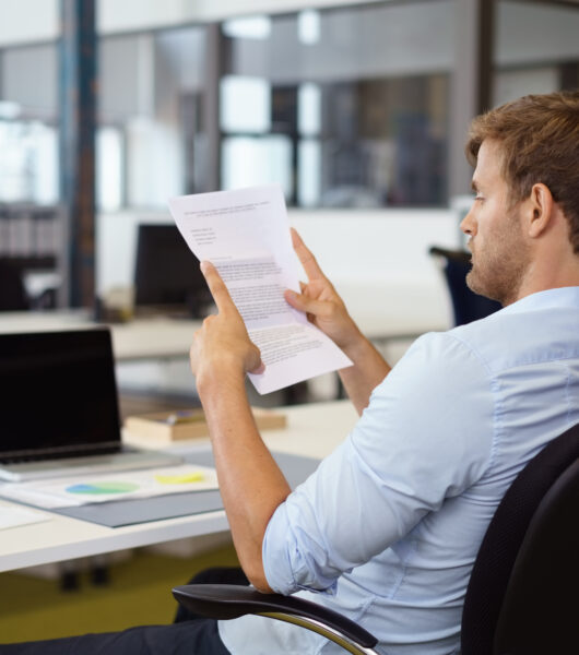 Businessman,Reading,A,Handheld,Typed,Document,At,His,Desk,In